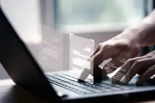 A person typing on a laptop, with the screen displaying job references in text format.