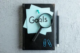 A notebook displaying career goals, accompanied by a pen, loose paper, and a clip-on pen on a workspace.