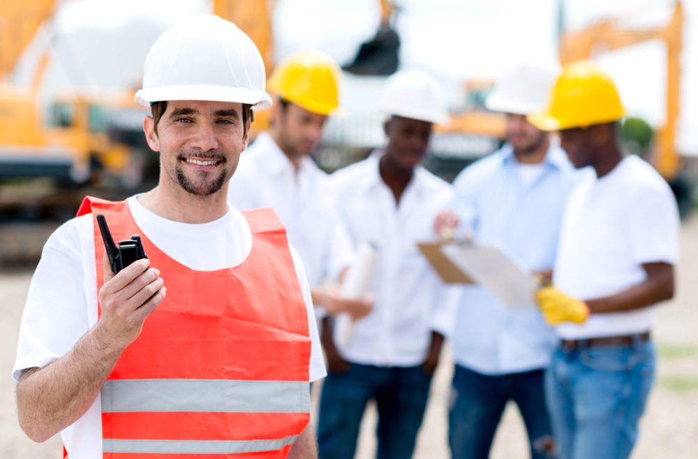 construction worker holding radio on construction site with workers in the background
