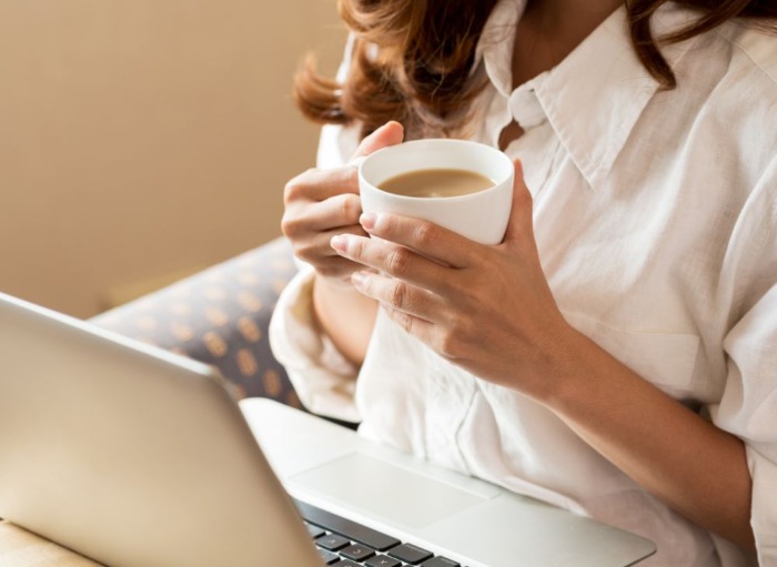 Woman ready something on her laptop whilst holding cup of tea