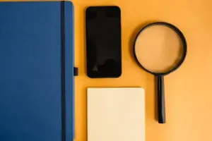 Job search tools displayed: a notebook, phone, and magnifying glass on a vibrant yellow background.