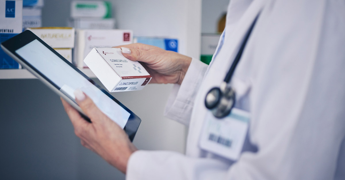 Pharmacist With A Box Of Pills And A Tablet In The Pharmacy