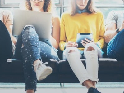 Two women sat on a seats looking at their phone