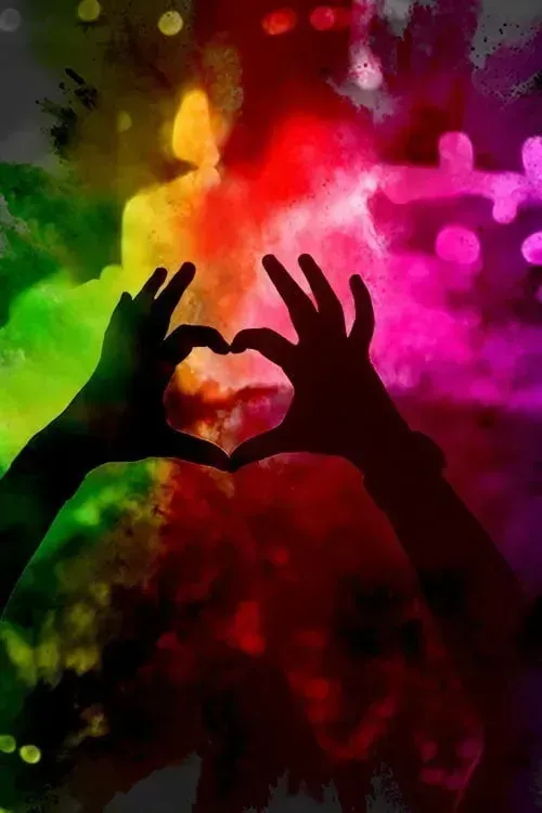 Hands making a heart shape with coloured powder in atmosphere.