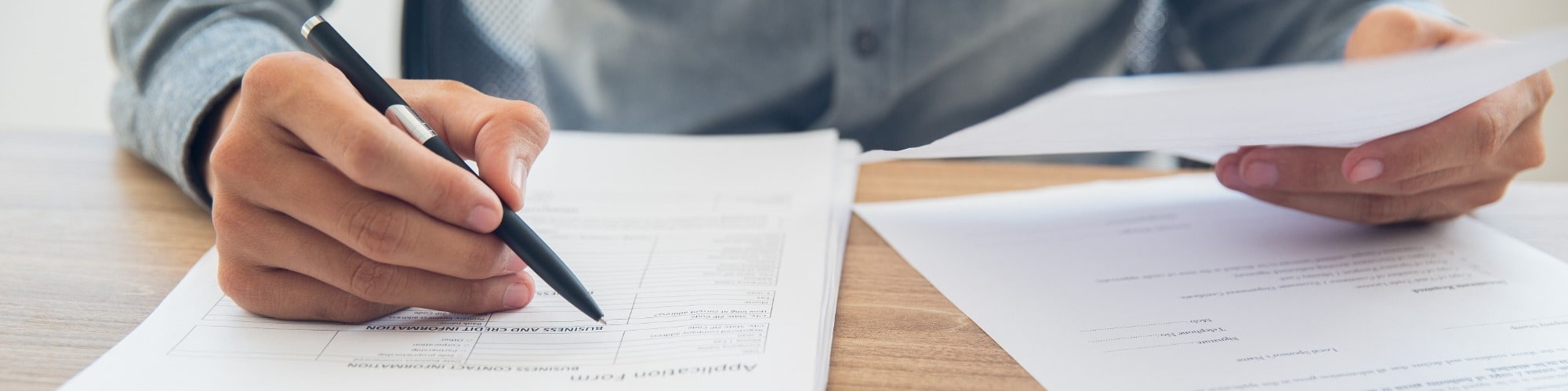 businessperson sitting at table holding ballpoint pen and papers and updating cv resume