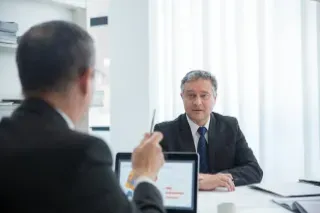 Two men in business attire seated at a table, engaged in a discussion, one identified as a manager.