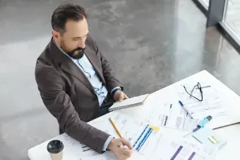 A man in a suit sits at a desk with papers and a coffee cup, demonstrating his skills as an interim finance specialist.
