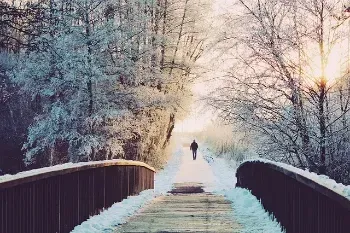 A person walks across a snowy bridge, enjoying a winter stroll to stay fit and combat the winter blues.