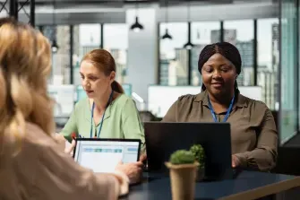Three women at a table with laptops, collaborating as temporary finance staff.