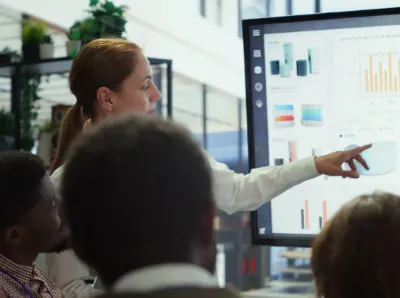A professional individual delivers a presentation in front of clients, using slides to enhance the discussion.