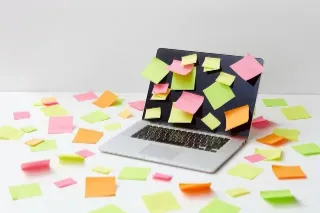 A laptop surrounded by various sticky notes on a white background, showcasing a method of note-taking and task management.