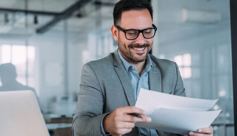 Business man smiling at paper documents whilst sat at a desk