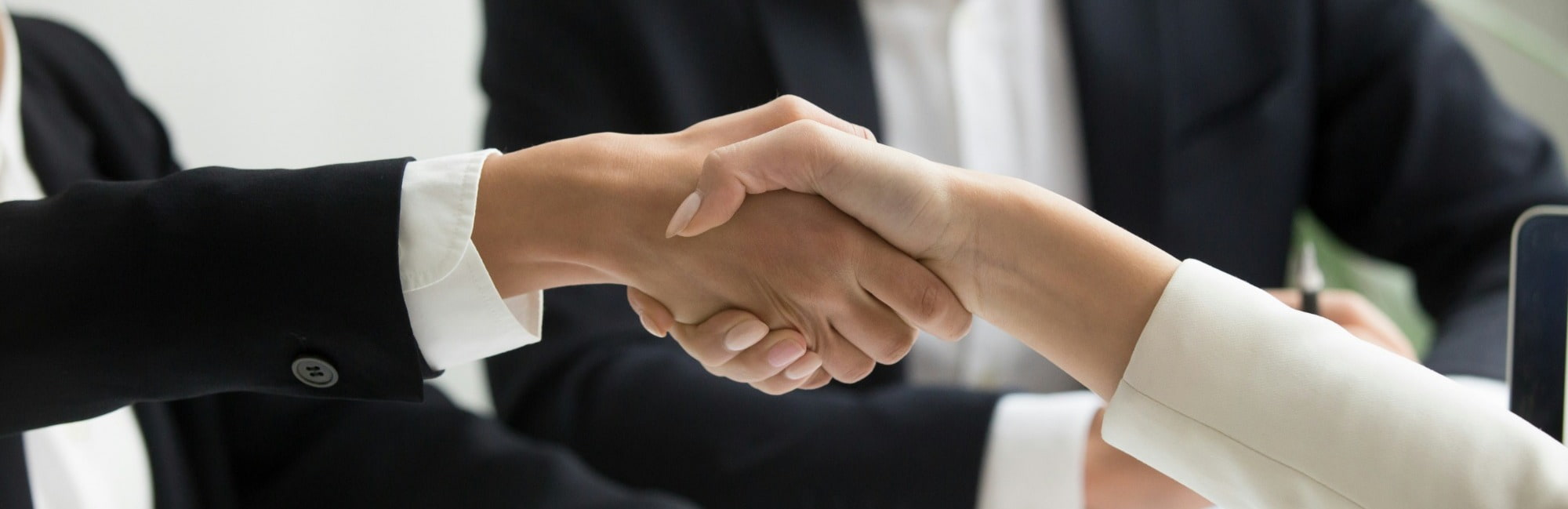 Two business professionals shake hands over a laptop during a job interview, symbolising agreement and collaboration.