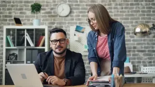 A man and woman engage with a laptop, illustrating effective collaboration and control at work.