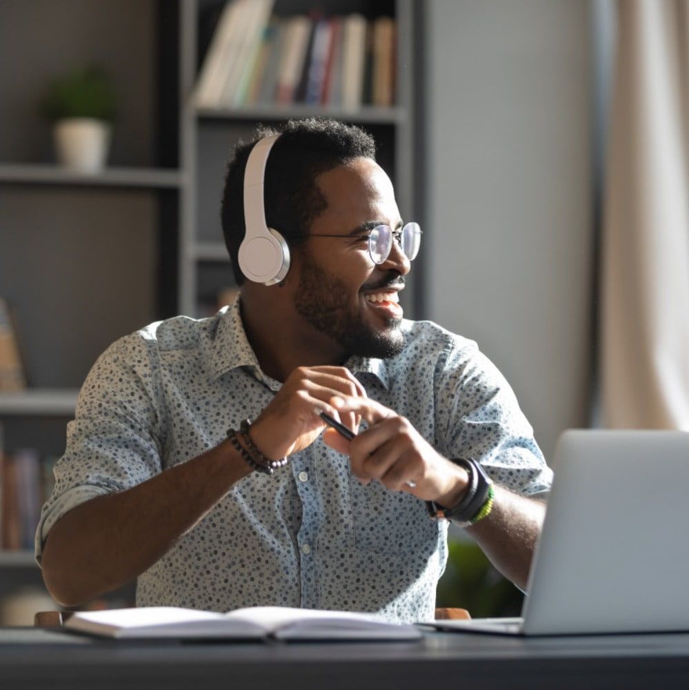 man sat with white headphones on looking off to the right, smiling