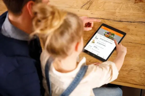 een klein meisje op schoot bij een man. Ze bestellen eten op de Ipad via de Just Eat Takeaway app