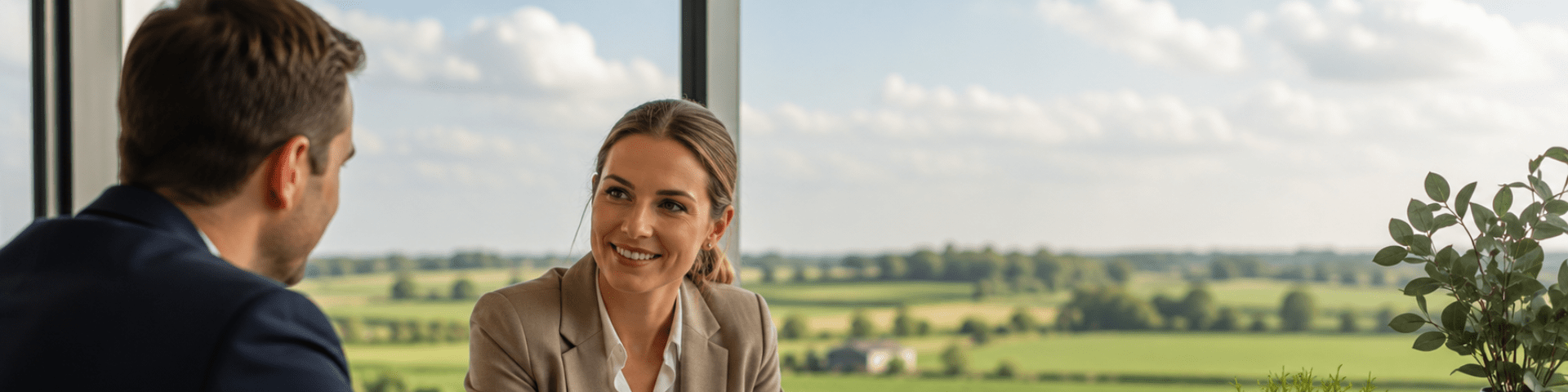 Two professionals in suits in a modern office with glass windows and green rural fields in the view