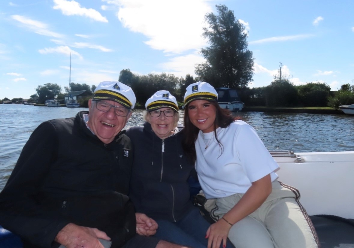 Three individuals wearing hats, smiling together on a boat, enjoying a sunny day on the water.