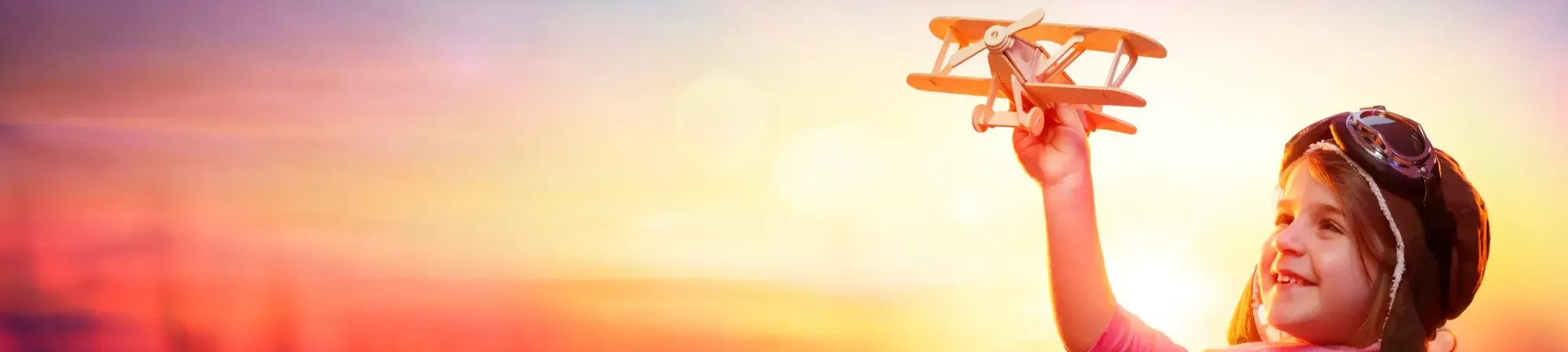 Little Girl In Goggles holding toy plane in the air