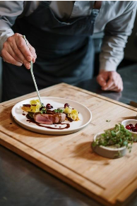 A chef preparing food on a plate  Description automatically generated