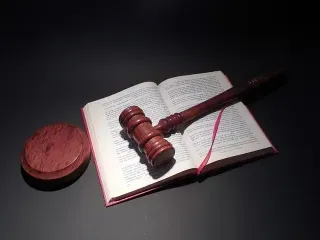 Wooden gavel resting on an open book, set against a black background, symbolising the phrase "judging a book by its cover."