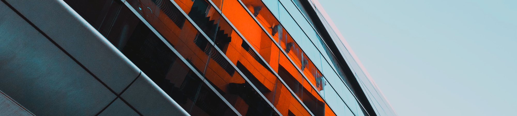 A large grey building with orange buildings reflected in the windows