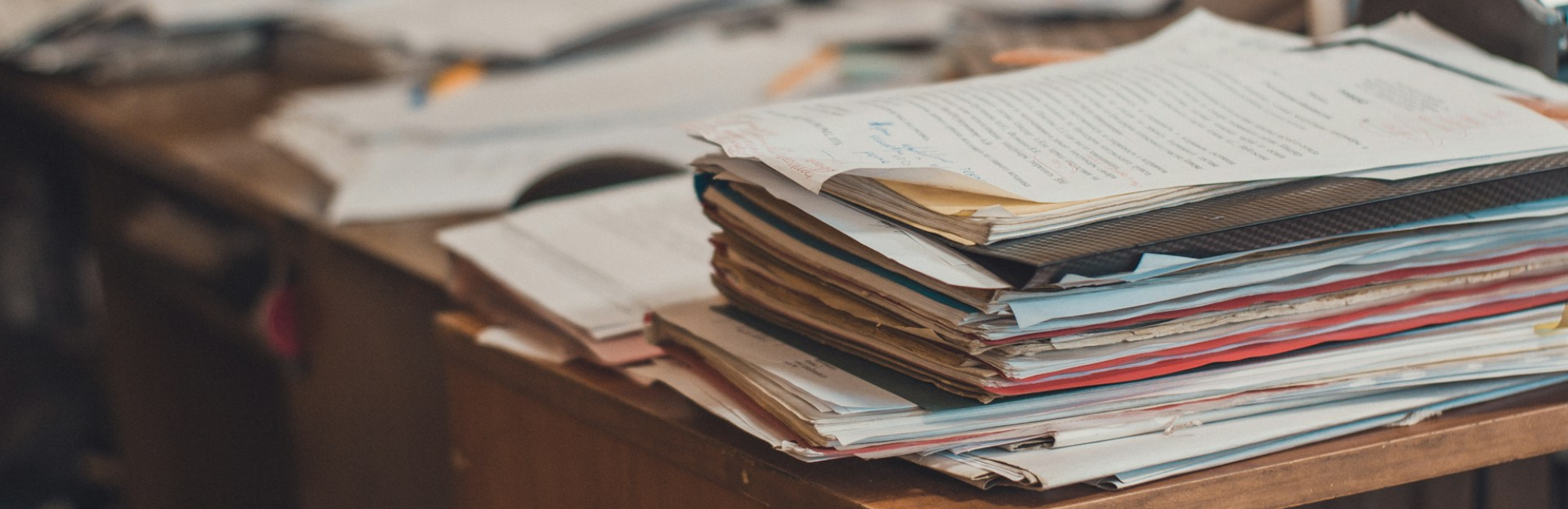 A stack of papers on a desk, indicating an increasing workload and the need for temporary assistance.