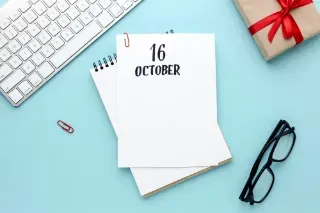 Top view of a notebook dated October 16, surrounded by a gift, keyboard, glasses, pen, phone, and calendar, with copy space.