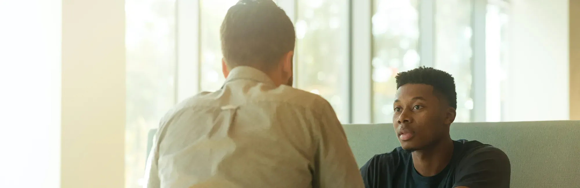 Two men engaged in conversation while seated at a table, displaying a friendly and attentive demeanor.