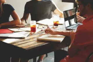 A group of interviewers gathered around a table, engaged in a panel interview while using laptops for notes.