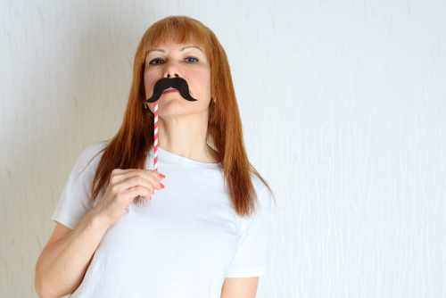 Young woman with gingger hair holding up a paper moustache prop