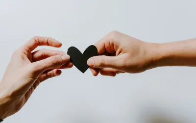 Two hands gently holding a black heart shape, symbolizing care and compassion.