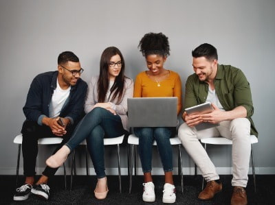 men and women sat on seats looking at laptop 