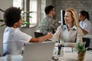 A woman and a man engage in a handshake at a desk, representing collaboration in a job-sharing arrangement.