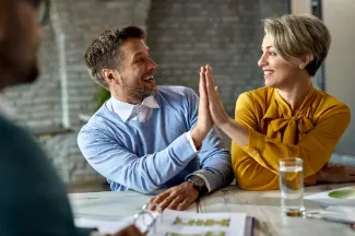 A man and woman give each other a high five, representing their supportive mentor-mentee relationship.