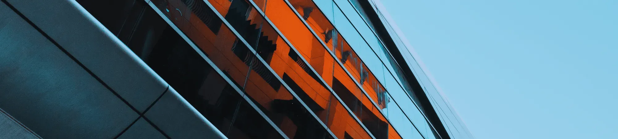 A modern grey building with orange buildings reflected in the windows