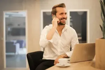 A professional man sitting at a desk, using a laptop while talking on the phone.