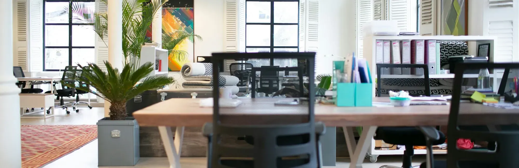 A spacious open office layout featuring desks, chairs, and collaborative work areas with natural light.
