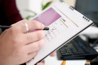 A person writes on a calendar with a pen, marking the date as 'day one'.