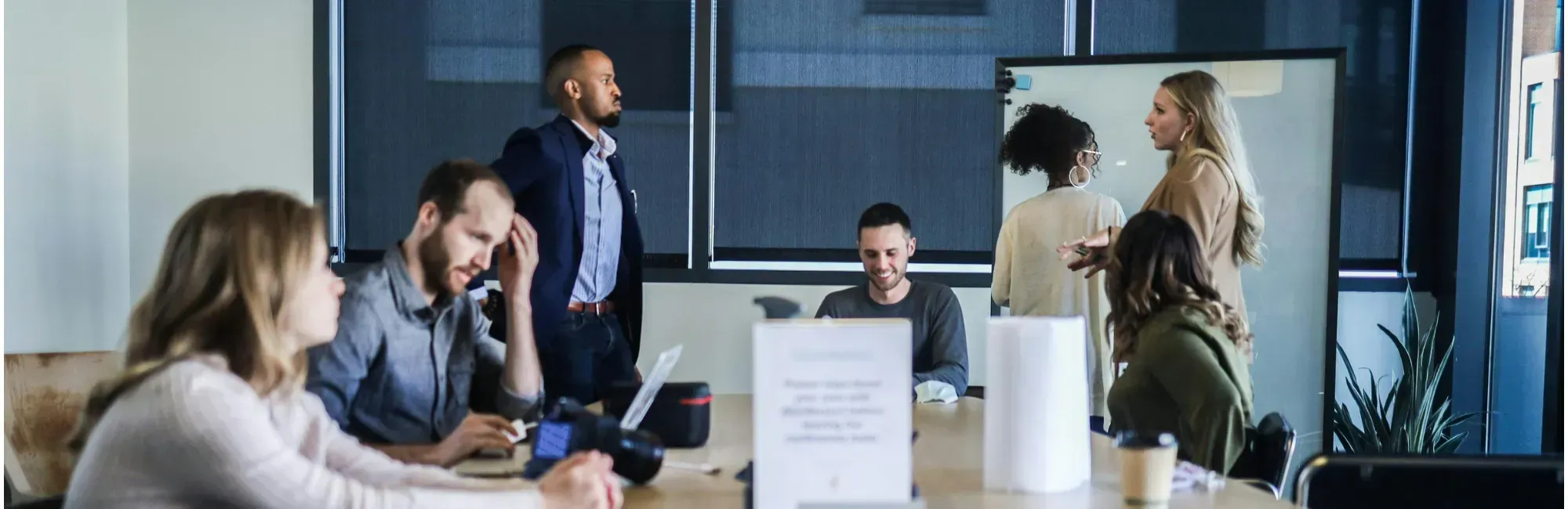 A group of professionals engaged in a meeting, with a large screen displaying presentation content in the background.