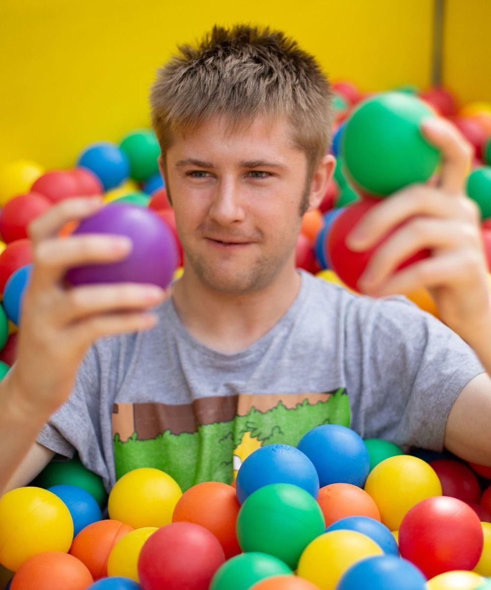 A man plays in a colourful ball pit and smiles