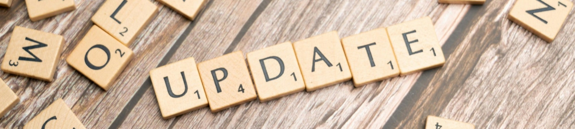 Scrabble tiles arranged to spell "update" on a rustic wooden table surface.