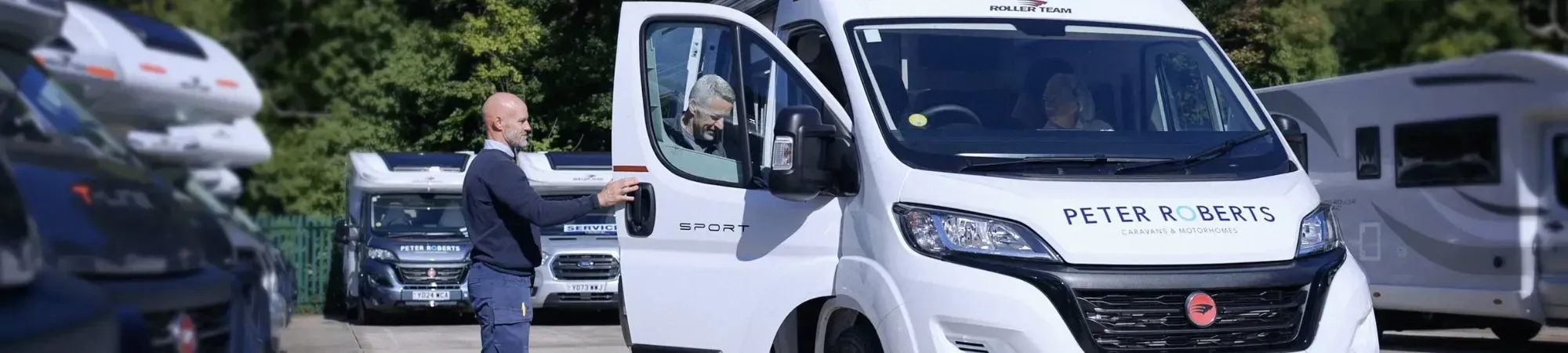 A man stands beside a white RV, showcasing Peter Roberts' motorhome in a sunny outdoor setting.