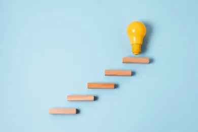 A glowing yellow light bulb rests on wooden blocks, representing inspiration and the next steps in your career.