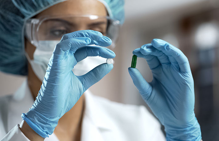 scientist holding one white pill and one green pill