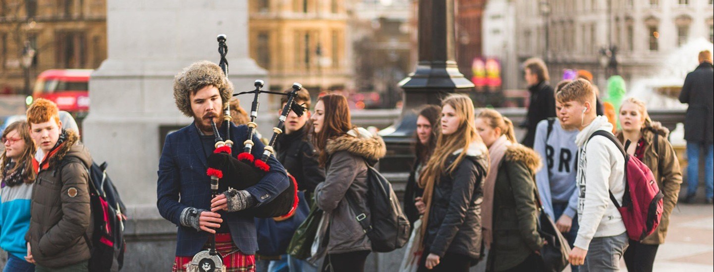 Man playing bagpipes in public, standing out in the crowd