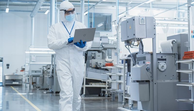 A person dressed in medical gear walking through a medical device centre using a laptop