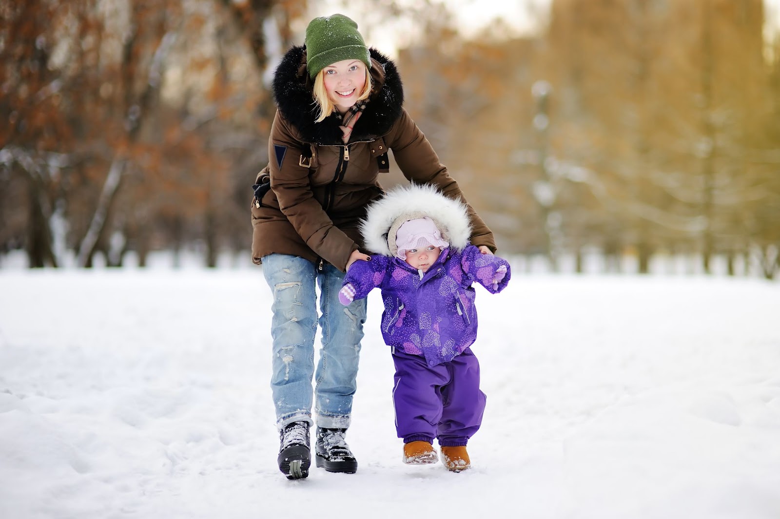 Nanny and child in purple coat walking on snowy ground.