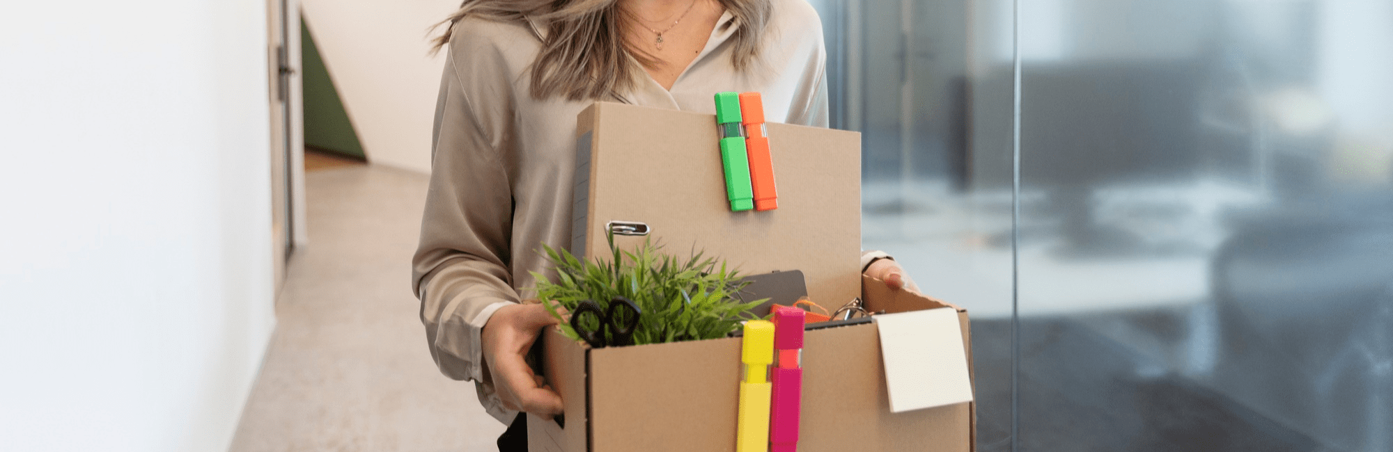 A woman carrying a box filled with a notepad and pencils, symbolising her transition to a new job in accountancy and finance.