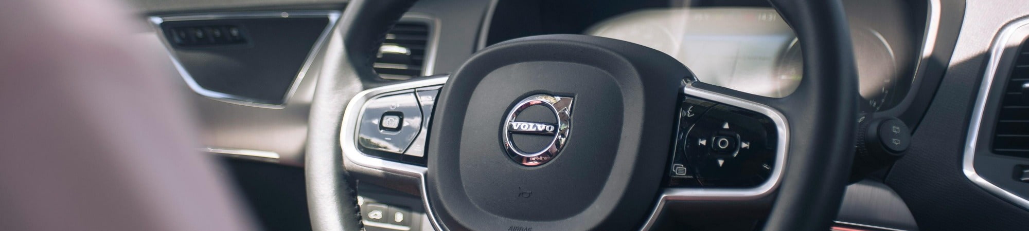 A man driving a Volvo car, focused on the road with the steering wheel prominently positioned in the center.